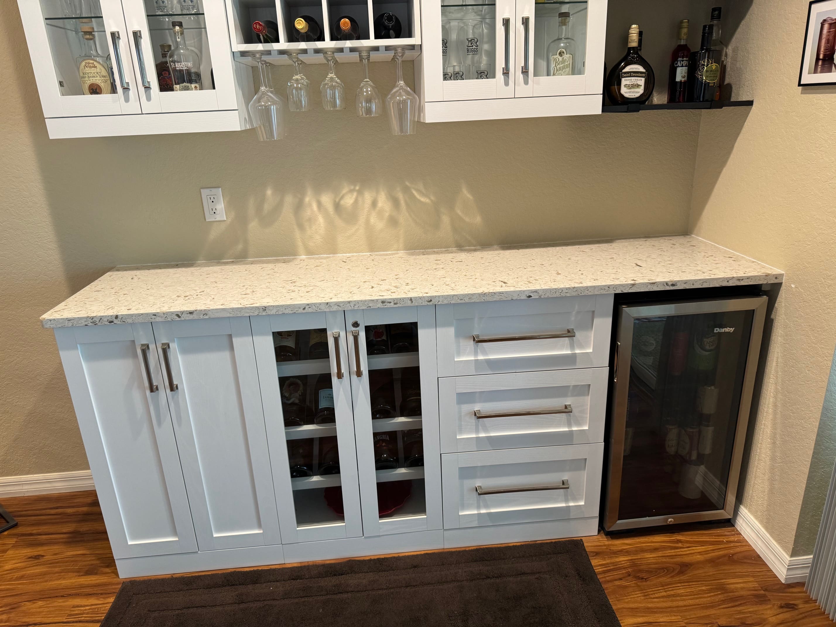 A white kitchen with wine bottles and glasses on the counter.