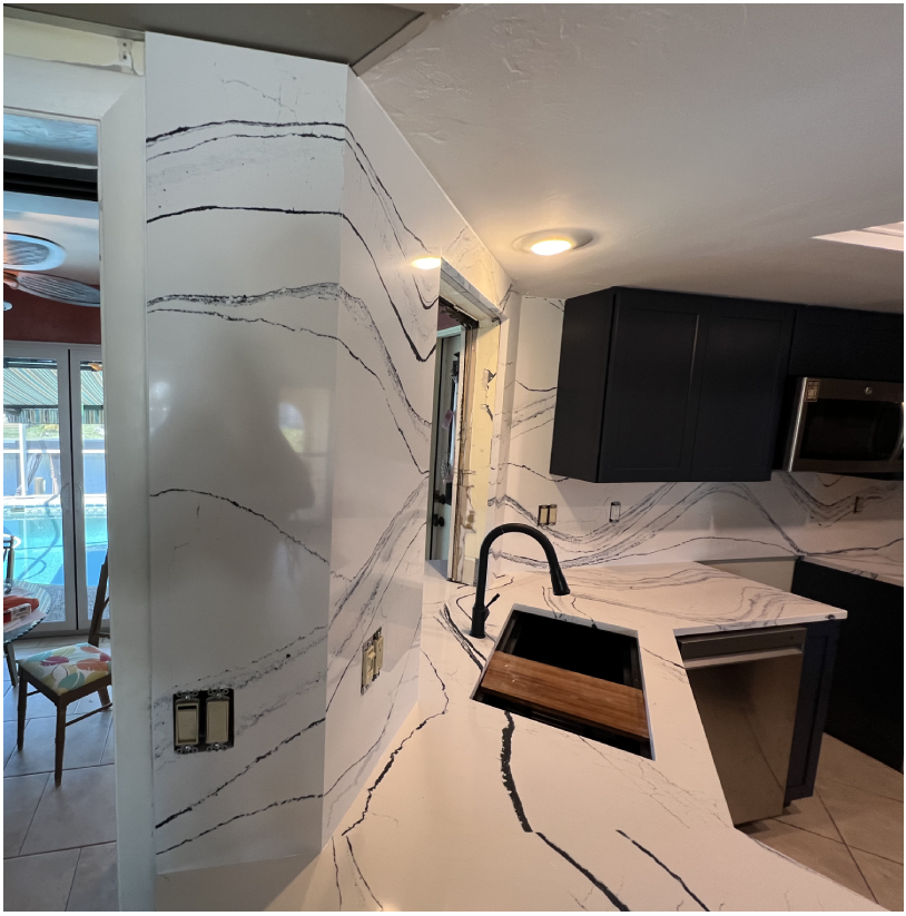 A kitchen with marble counter tops and black cabinets.