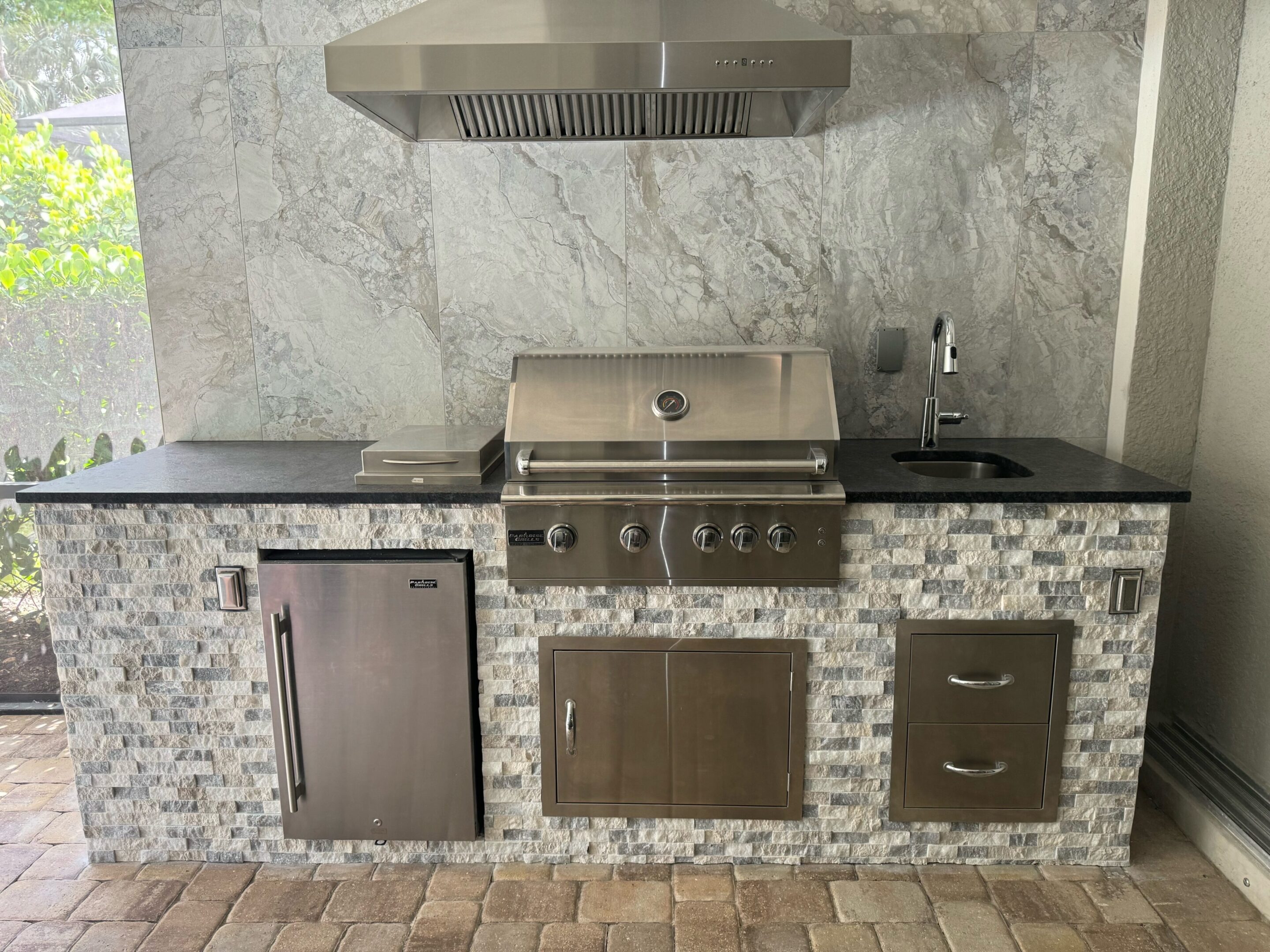 A grill and refrigerator in the middle of an outdoor kitchen.